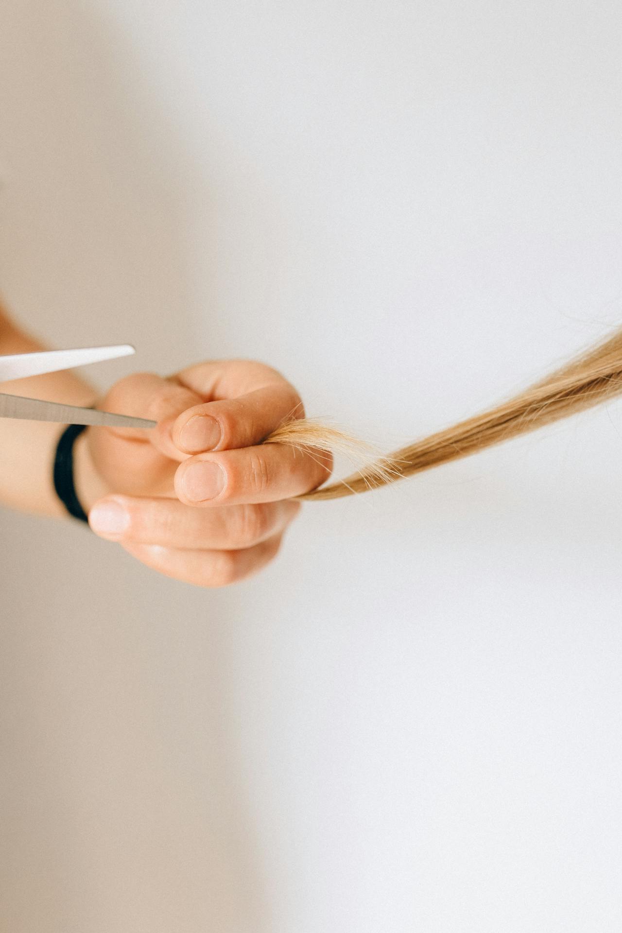 picture of a hand with scissors about to cut a split ends from a section of blonde hair