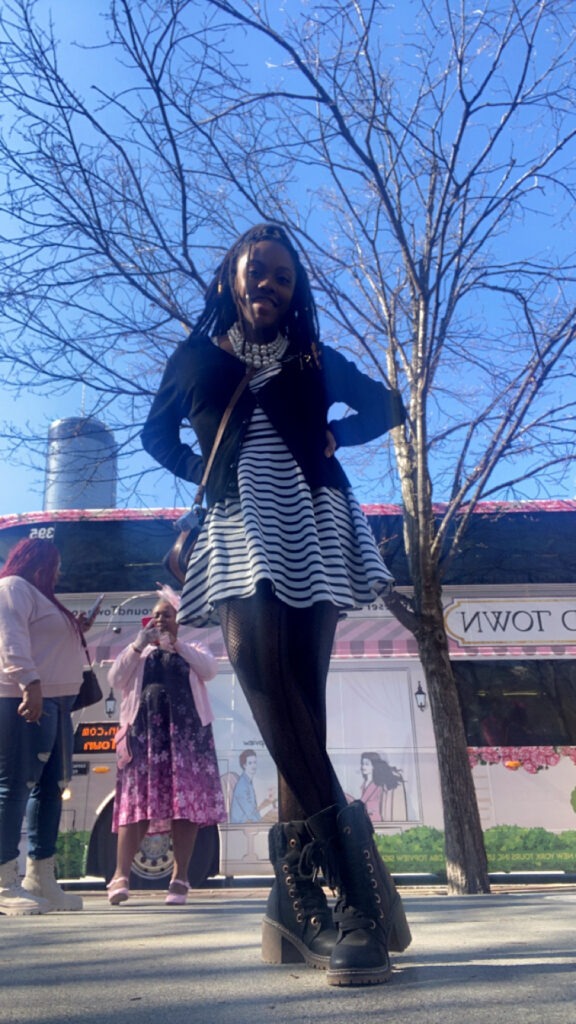 ash in front of the tea around town bus in atlanta ga with a short black and white dress, black sweater, black fishnets, and black boots with heels