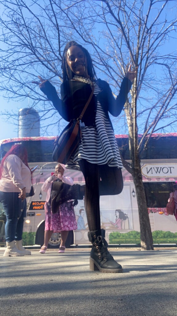 ash in front of the tea around town bus in atlanta ga with a short black and white dress, black sweater, black fishnets, and black boots with heels