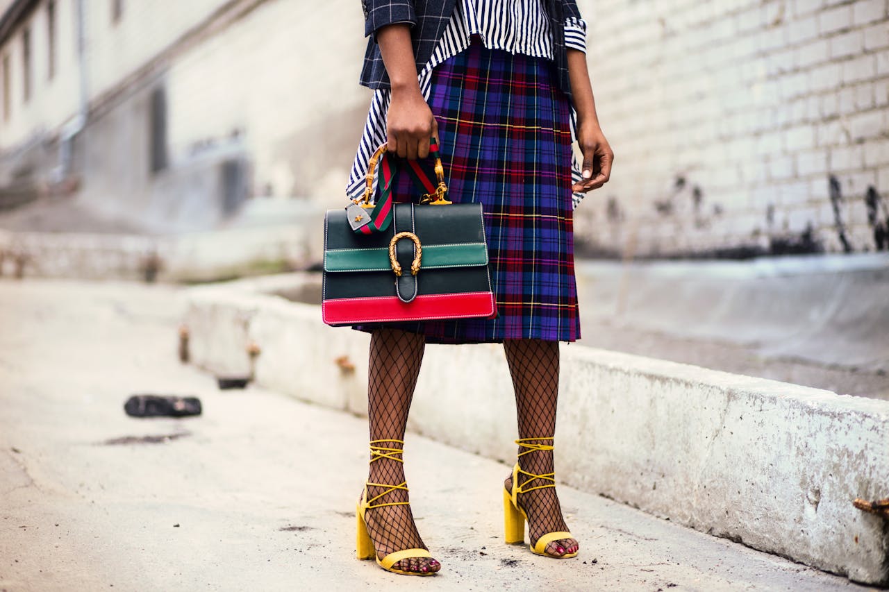 black lady with a colorful sense of style. fashion style with a blue plaid skirt, black fishnets, yellow open toe shoes, black and white strip blouse and a black red and green handbag